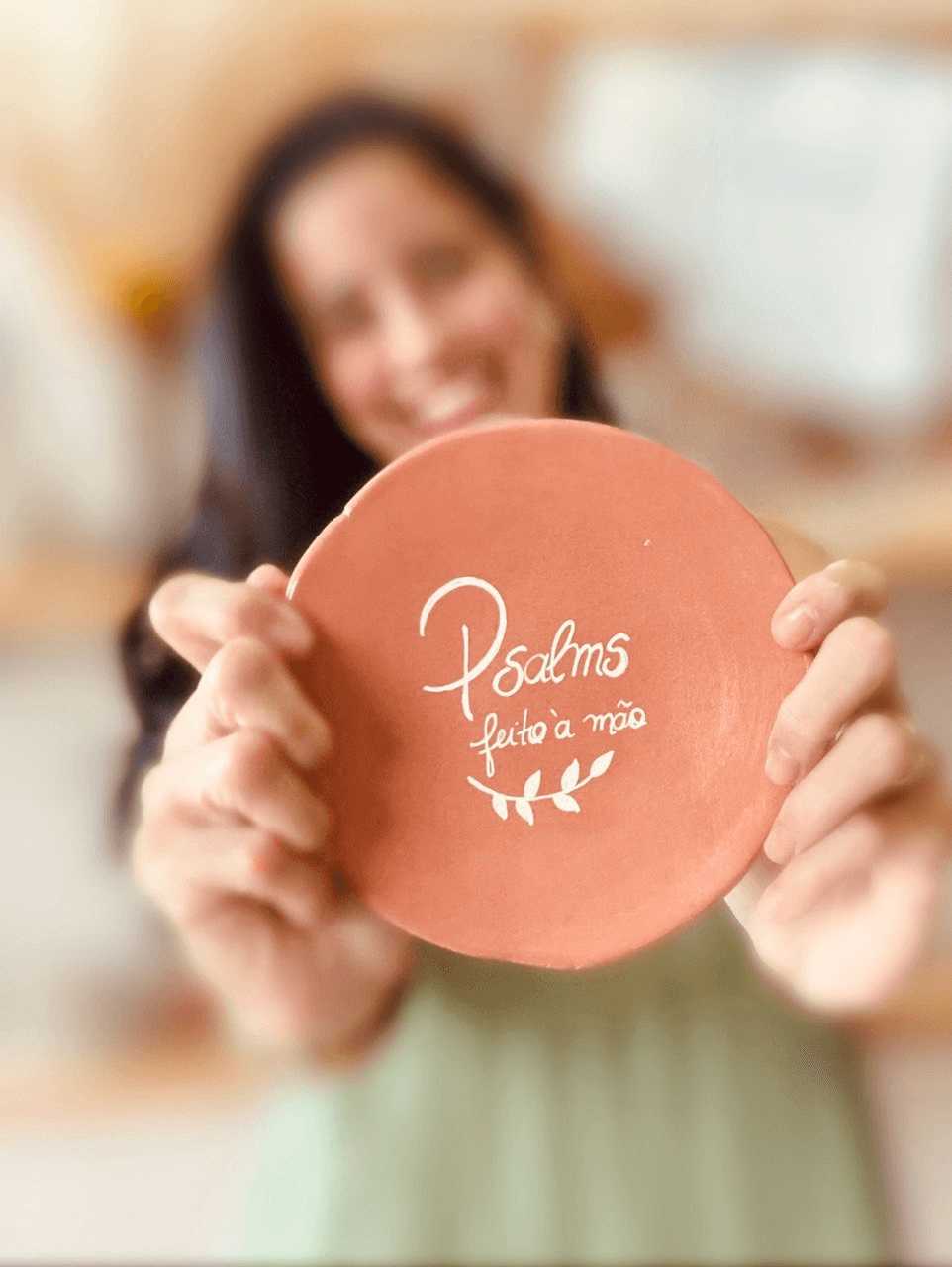 Margareth sorrindo enquanto segura uma peça de cerâmica artesanal escrito Psalms.
